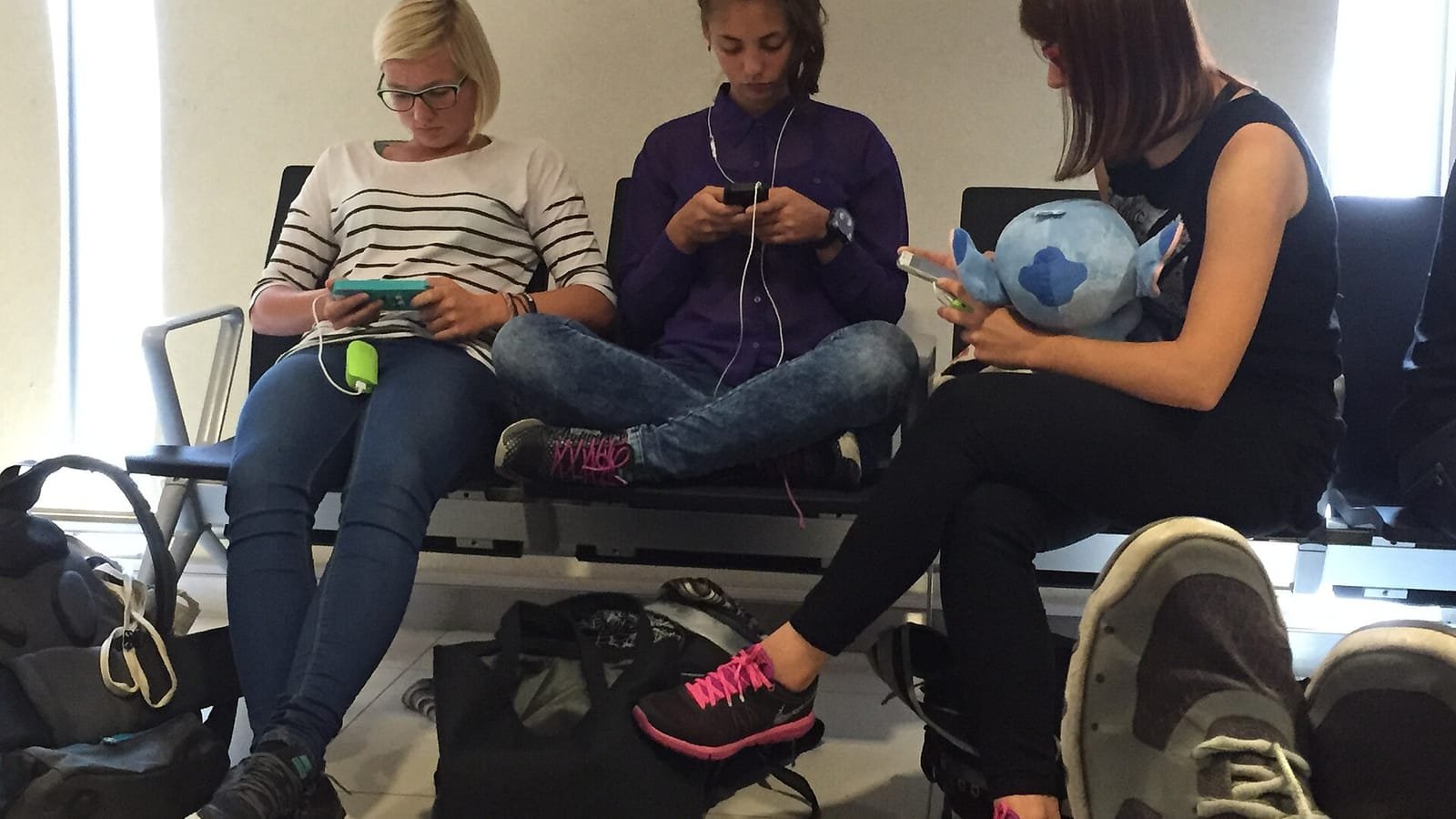 Tres jóvenes sentadas en un banco de sala de espera, cada una mirando su teléfono móvil
